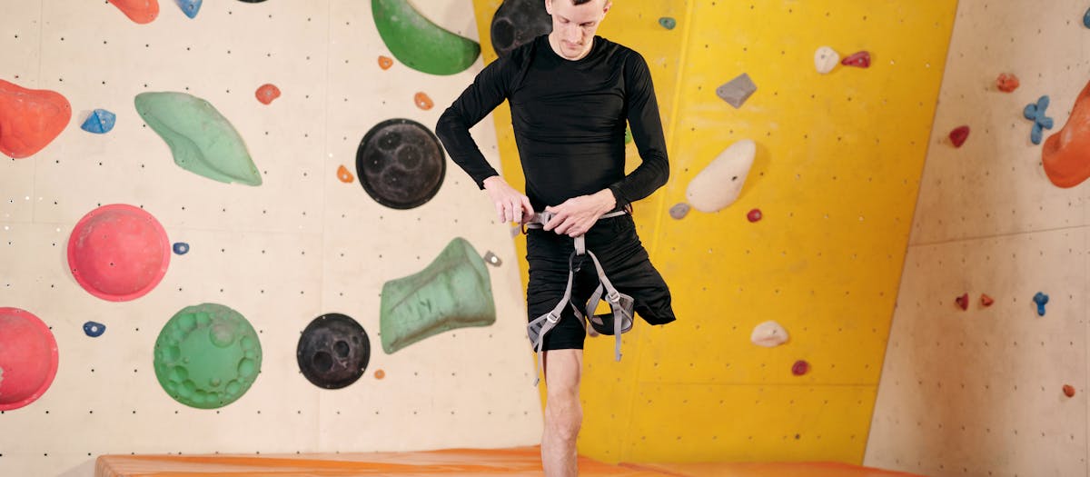Amputee climber adjusting gear for indoor rock climbing on a vibrant wall.