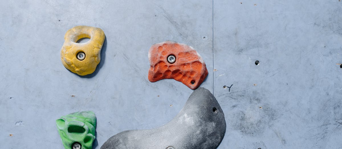 Detailed close-up of colorful climbing holds on an indoor gray rock climbing wall.