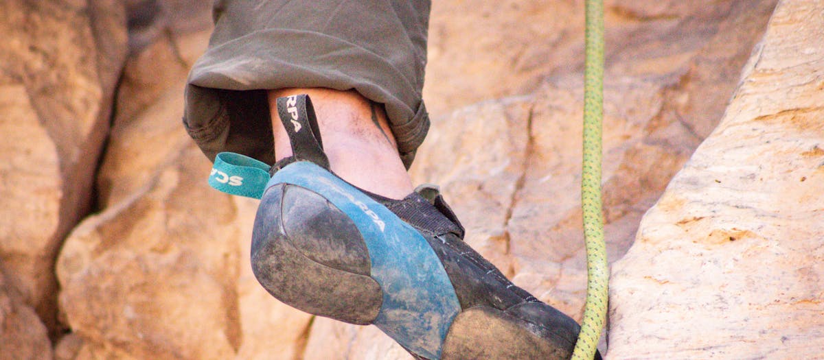 Close-up image of a climber's foot in a rock climbing shoe gripping a rocky surface.